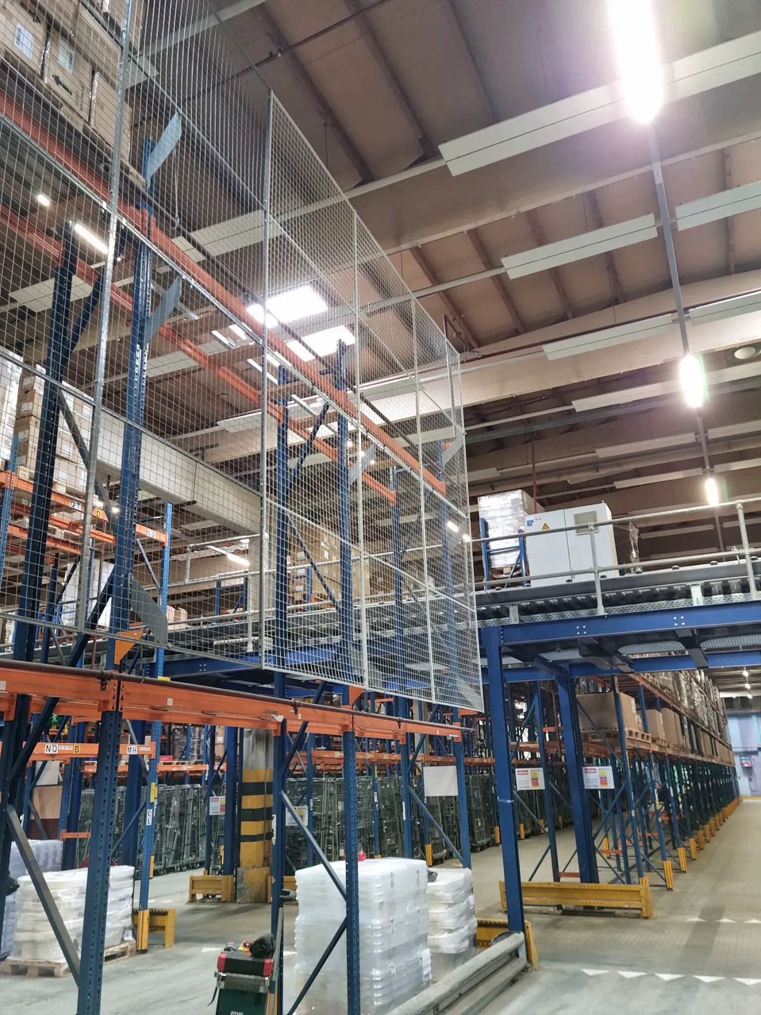 Magazijnstellingen met veiligheidshekken en opgestapelde goederen in een industrieel magazijn