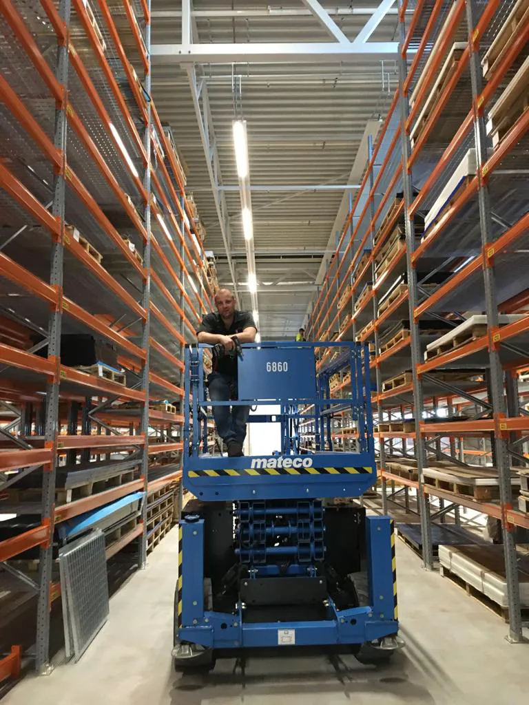 Een werknemer op een hoogwerker tussen magazijnstellingen met stalen planken